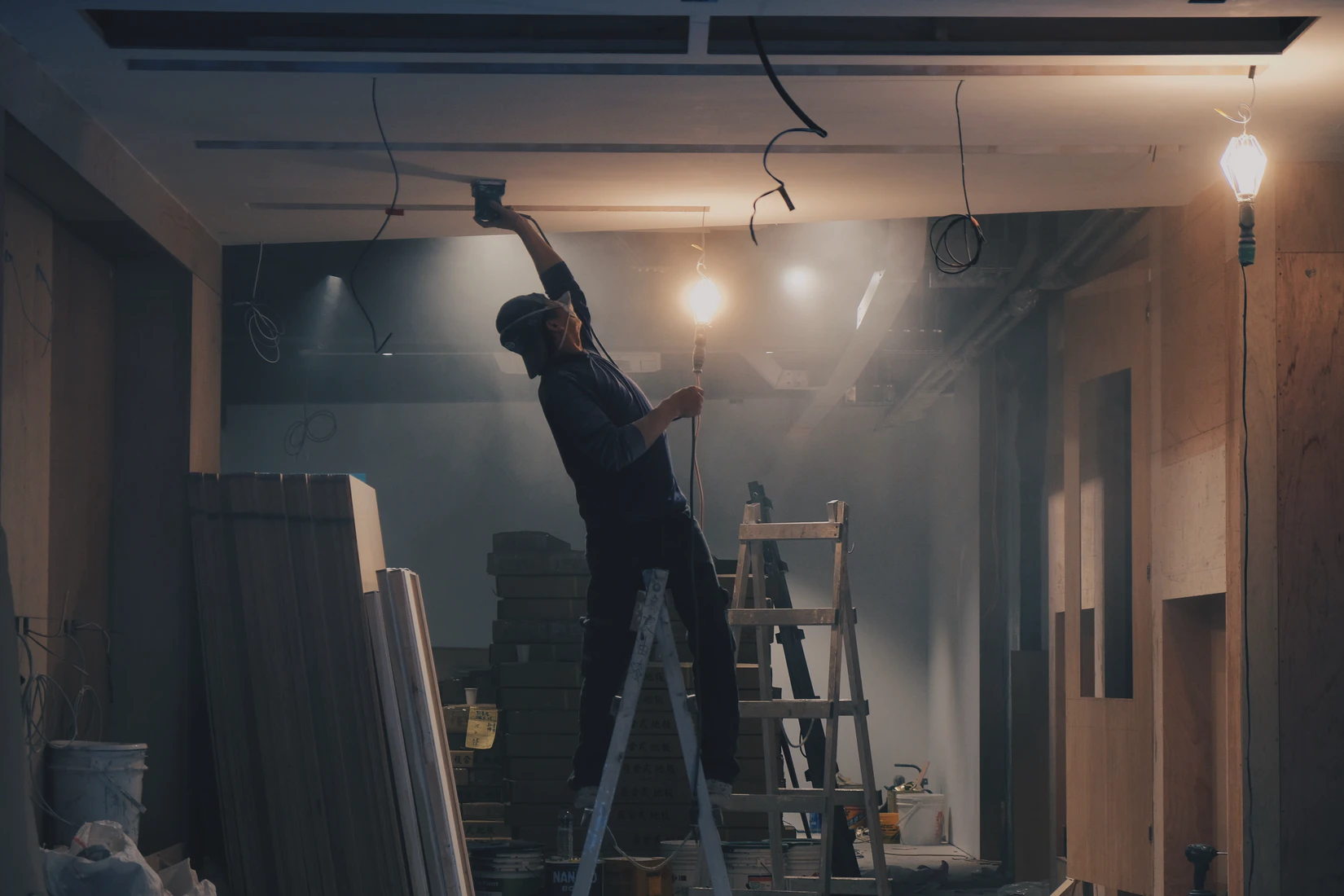 a man on a ladder doing a house renovation holding a light and painting the ceiling