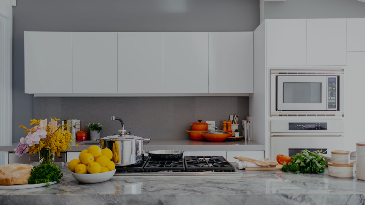 A white and grey modern kitchen with a cooktop, lemons, flowers and orange pots