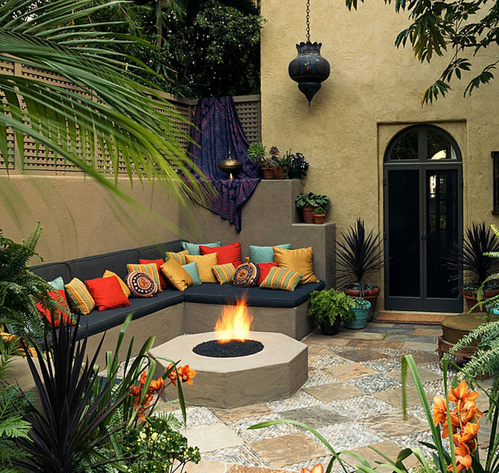 An outdoor fireplace in a garden with couches and multicoloured pillows.