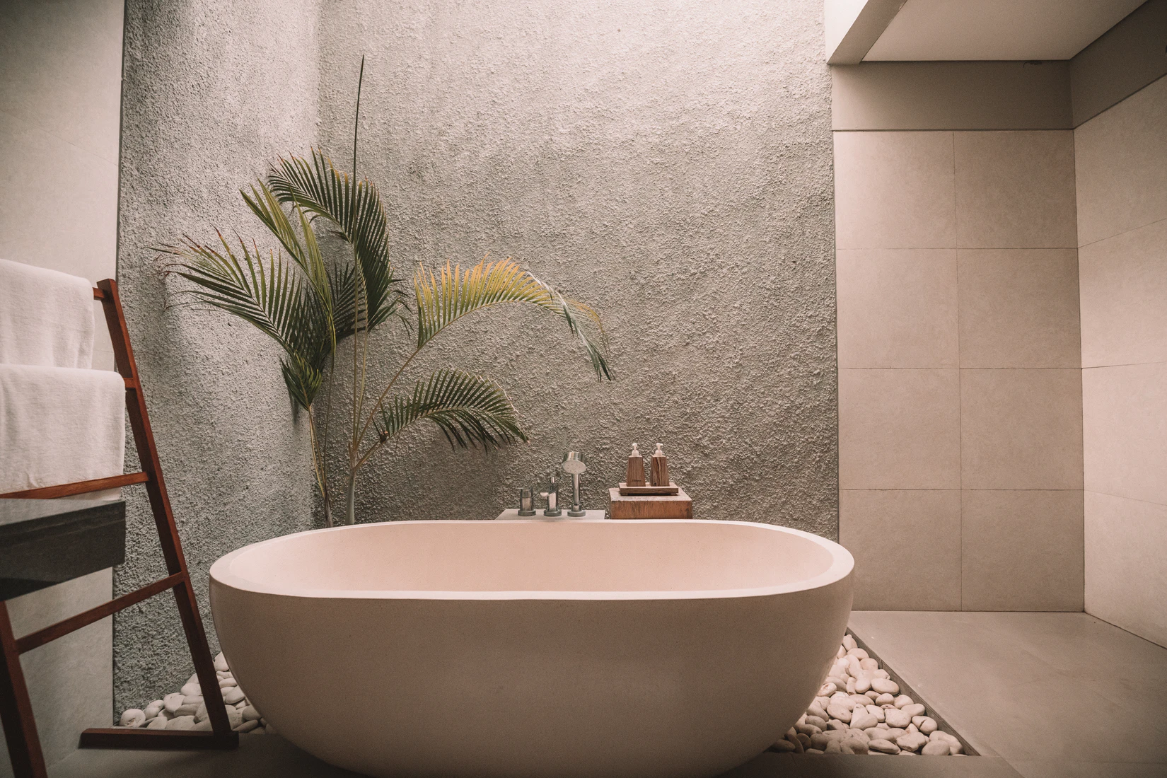Tiled creme bathroom with a plant in the corner and a modern bathtub in the middle