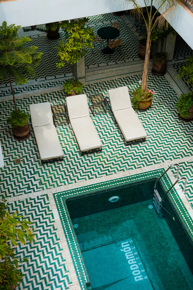 three white chairs next to a pool with green and white tiles